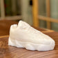 The Y500 – White Sneaker Candle – Small, hand-poured and wax-like, sits on a wooden surface—perfect for adding unique style and a subtle fragrance to any space.