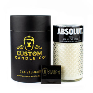 The Recycled Vodka Candle – Absolut is a hand-poured soy candle in a repurposed Absolut vodka glass, packaged in a black cylindrical box with a business card displayed in front.