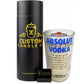 The Recycled Blue Letter Vodka Candle, made from a repurposed Absolut Vodka bottle, is displayed with a black cylindrical Custom Candle Co. box and a matching small black matchbox.