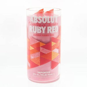 A clear glass holds a pink drink with geometric red and orange patterns and "Absolut Ruby Red" text, inspiring the Recycled Vodka Candle – Absolut Red Ruby, perfect for a custom or hand-poured soy vodka candle design.