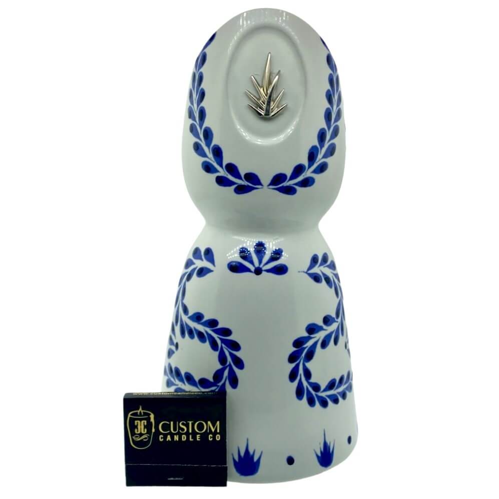 The Recycled Azul Tequila Curve Cut Candle, a hand-poured soy candle in a white ceramic bottle with blue floral patterns and a silver emblem, offers an elegant, cruelty-free touch.