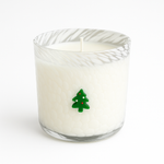 The Christmas Tree Glass Candle features a white holiday candle in a textured glass holder with a small green Christmas tree on the front. A perfect festive accent for your home décor, shown against a plain white background.