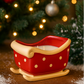 The Sleigh Candle, a red ceramic candle with gold polka dots, sits on a wooden surface. Festive decor and twinkling lights in the background enhance its warm holiday glow, making it a charming addition to your Christmas setting.