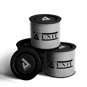 Four cylindrical containers labeled "The Unit - Promotional Tin Candle," three stacked and one lying down, with black text on white background and black lids—ideal as a custom candle or for promotions.
