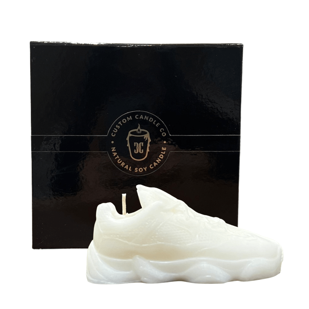 The Y500 – White Sneaker Candle – Small is shown in front of a black "Custom Candle Co Natural Soy Candle" box. Hand-poured, this candle adds a playful accent to any space.