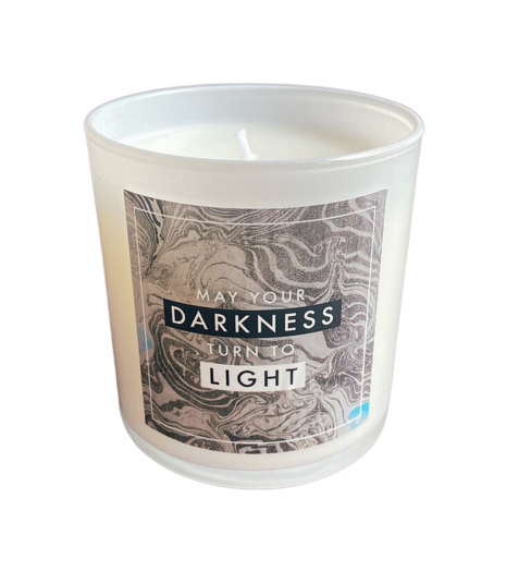 A quote candle in a white container with the phrase "May your Darkness Turn Into Light"