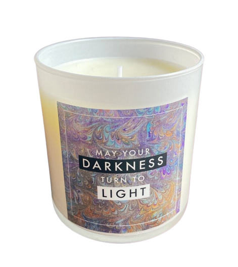 A white glass container with white wax with the quote "May your darkness turn into light."