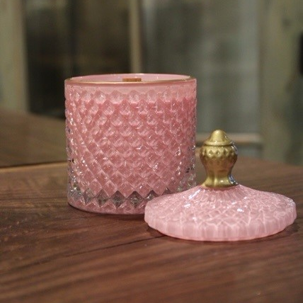 An elegant pink crystal scented candle with a gold lid on a wooden table.