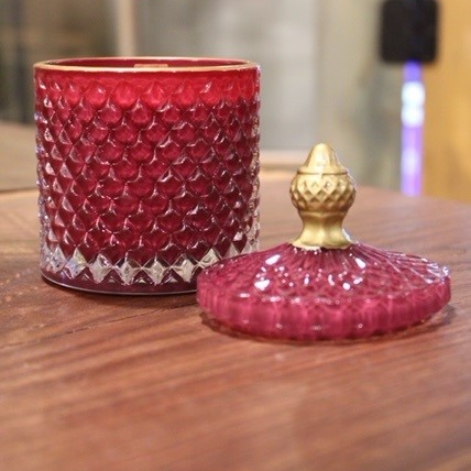 An Elegant Red Crystal Scented Candle with a gold lid sits on a wooden table.