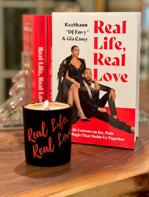 The Real life, Real Love Scented Candle with a copy of the book "Real Life, Real Love: Life Lessons of Joy, Pain and Magic that Holds Us Together" by RaasShaun "DJ Envy" and Gia Casey.