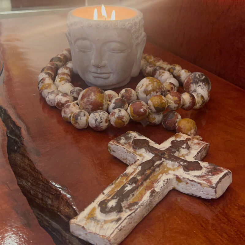 A rosary and candle on a wooden table adorned with a Pottery Buddha Head, 3 wick, Sage Scented.