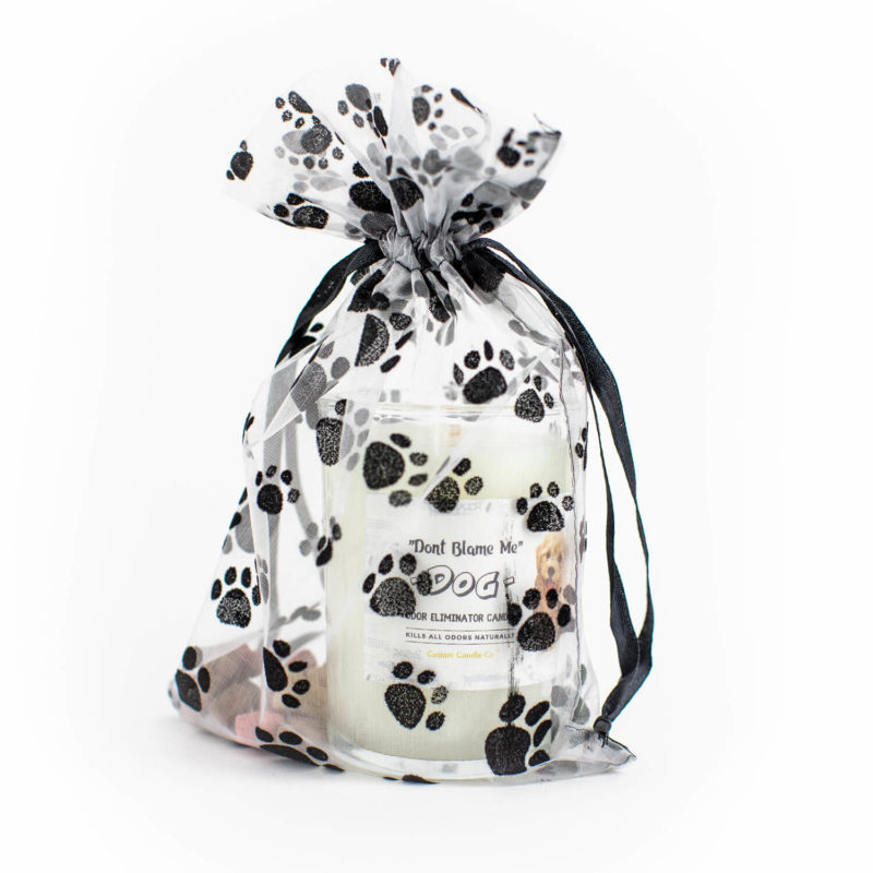 A "Don't Blame Me" Dog Candle Odor Eliminator candle in a white mesh bag decorated with black paws.