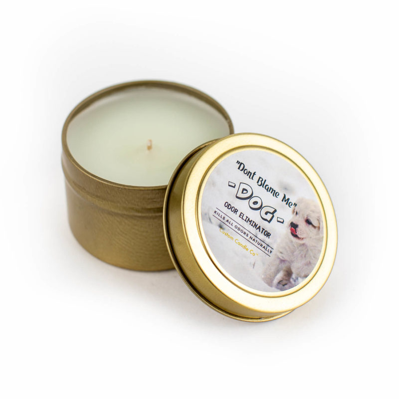 A gold "Don't Blame Me" Dog Tin Candle Odor Eliminator with a white dog on it.