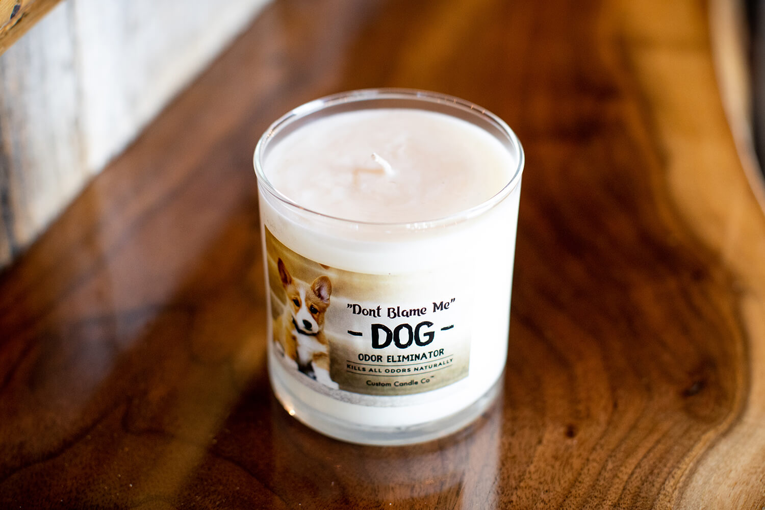 A small "Don't Blame Me" Dog Candle Odor Eliminator sits on a wooden table.