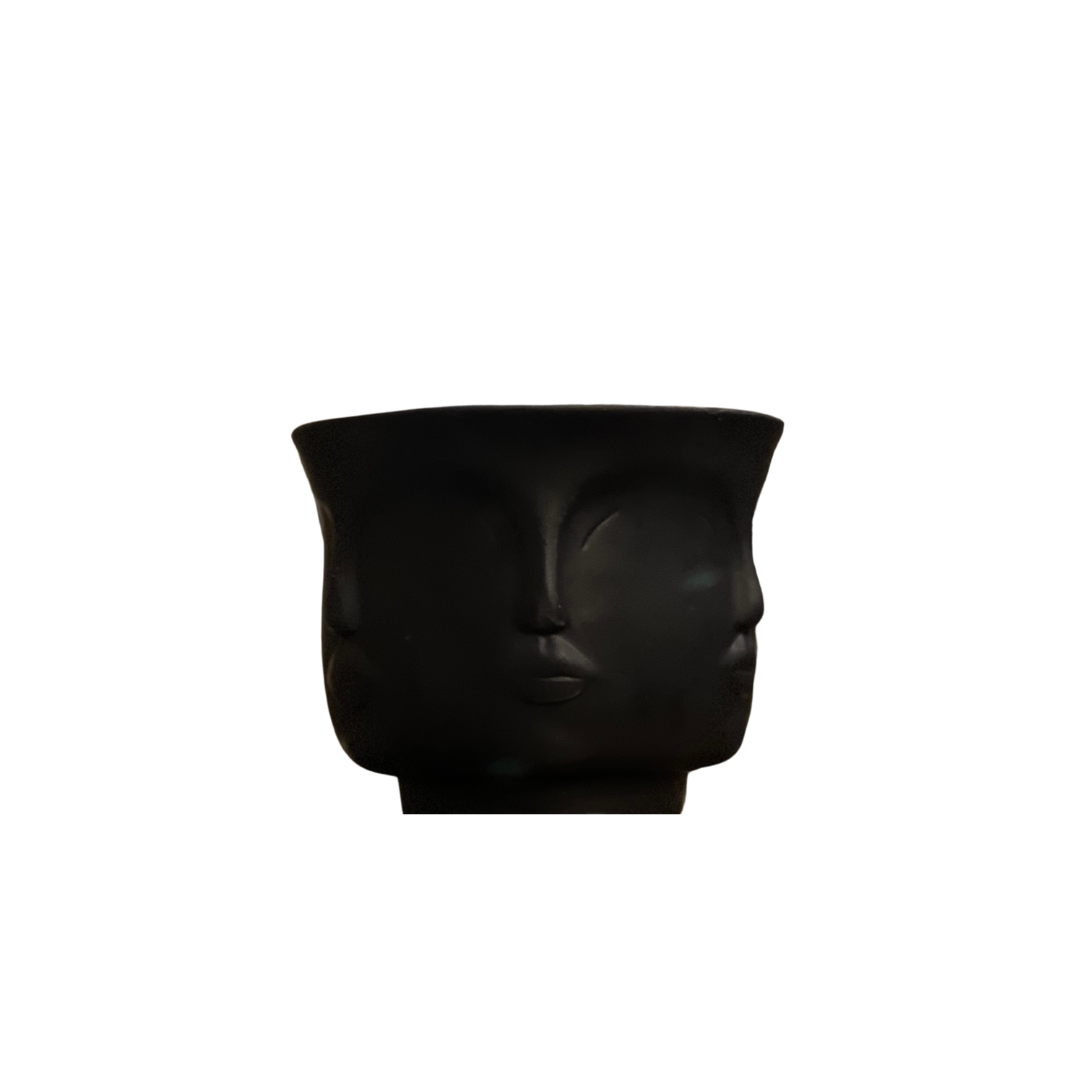 A black vase with a Buddha Head Candle, Sage Scented on it.